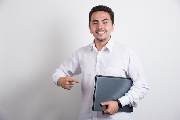 Empresario apuntando portátil con expresión feliz sobre fondo blanco.
