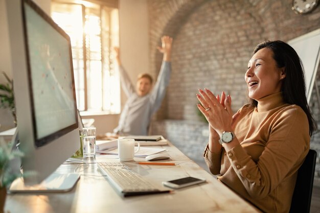 Empresario asiático y su compañero de trabajo celebran el éxito empresarial mientras usan la computadora en la oficina