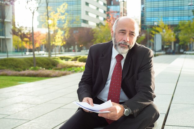 Empresario cansado sentado con informes al aire libre