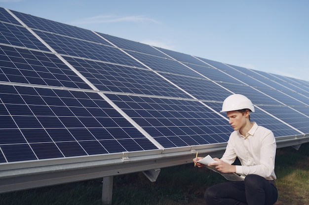 Empresario en un casco blanco cerca de batería solar