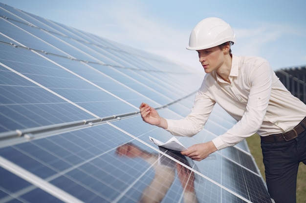 Empresario en un casco blanco cerca de batería solar