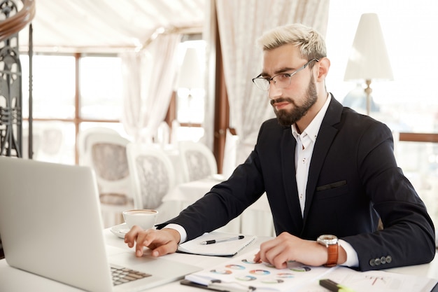 Foto gratuita empresario enfocado que usa lentes está trabajando en la computadora portátil en el restaurante