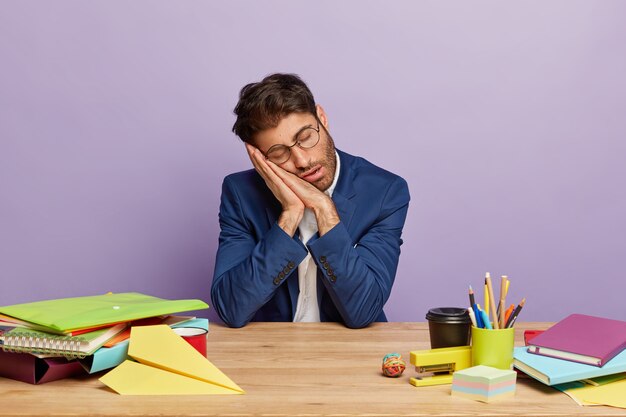 Empresario con exceso de trabajo cansado sentado en el escritorio de oficina