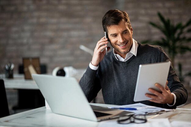 Empresario feliz comunicándose por teléfono móvil mientras trabaja en el panel táctil en la oficina