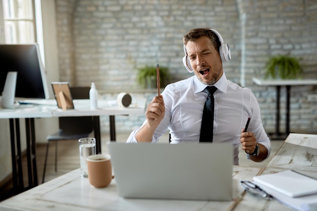 Empresario feliz divirtiéndose mientras escucha música y canta en la oficina