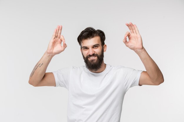 El empresario feliz de pie y sonriendo contra la pared blanca