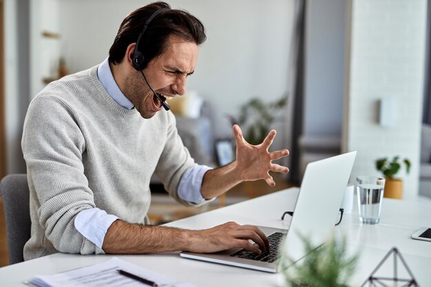 Empresario frustrado gritando mientras trabaja en una computadora y tiene algunos problemas