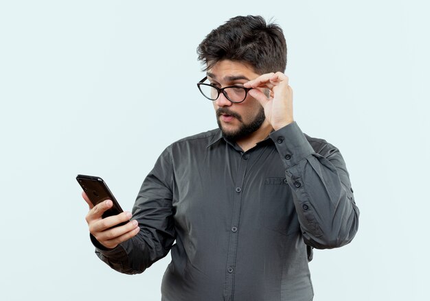 empresario con gafas sosteniendo y mirando el teléfono aislado en blanco