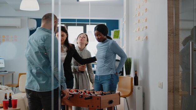 El empresario gana el juego de fútbol en el futbolín, jugando con la mujer afroamericana después del trabajo. Compañeros de trabajo disfrutando del ocio con pizza y botellas de cerveza para divertirse con la actividad.