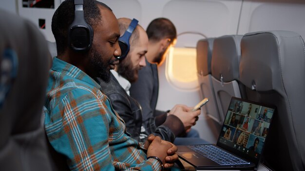Empresario hablando en una conferencia de videollamadas en un avión que vuela en clase económica. Usando una llamada de teleconferencia remota en línea en una computadora portátil, viajando con una reunión por Internet.