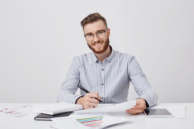 Empresario hombre barbudo sonriente ocupado tiene lápiz y documento