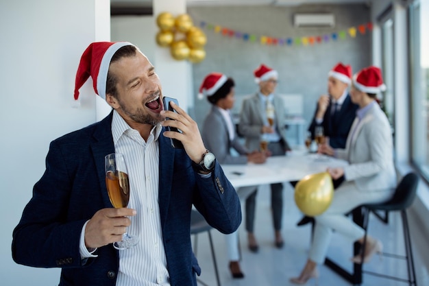 Empresario juguetón firmando mientras usa un teléfono inteligente en la fiesta de Navidad en la oficina