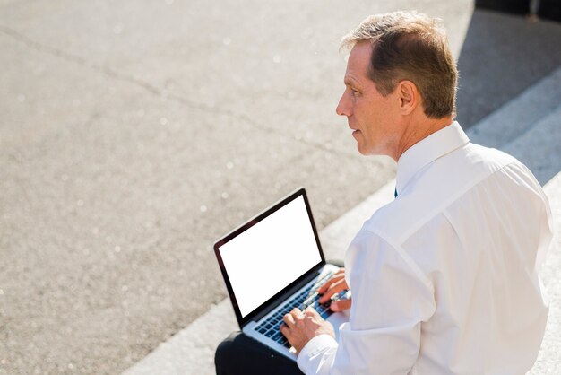 Empresario maduro usando laptop con pantalla blanca en blanco