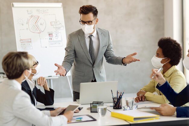 Empresario con mascarilla protectora hablando con compañeros de trabajo en una reunión en la oficina