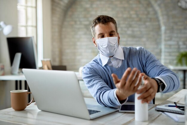 Empresario masculino que usa desinfectante de manos mientras trabaja en la oficina durante la epidemia de coronavirus