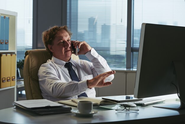 Empresario de mediana edad hablando por teléfono y gesticulando