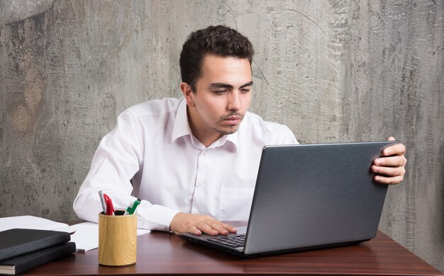 Empresario mirando a la computadora portátil y sentado en el escritorio. Foto de alta calidad