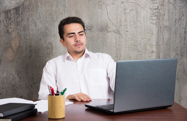Empresario mirando a la computadora portátil y sentado en el escritorio. Foto de alta calidad
