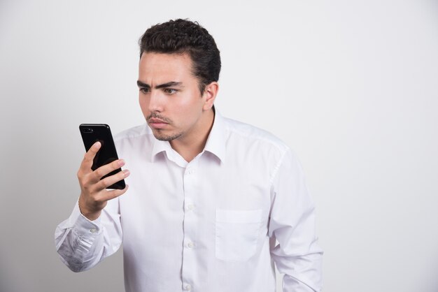 Empresario mirando intensamente el teléfono sobre fondo blanco.