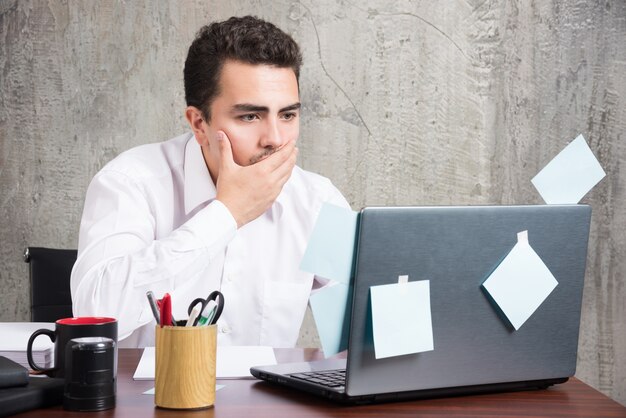 Empresario mirando portátil mientras sostiene su boca en el escritorio de oficina.