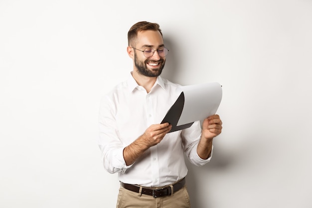 Empresario mirando satisfecho con los documentos, leyendo el informe y sonriendo, de pie