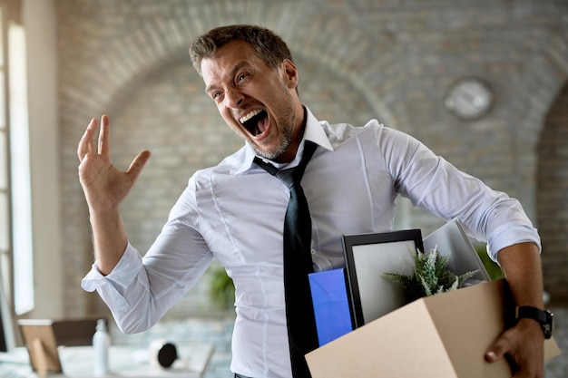 Empresario molesto gritando mientras cargaba sus pertenencias y salía de la oficina después de perder su trabajo