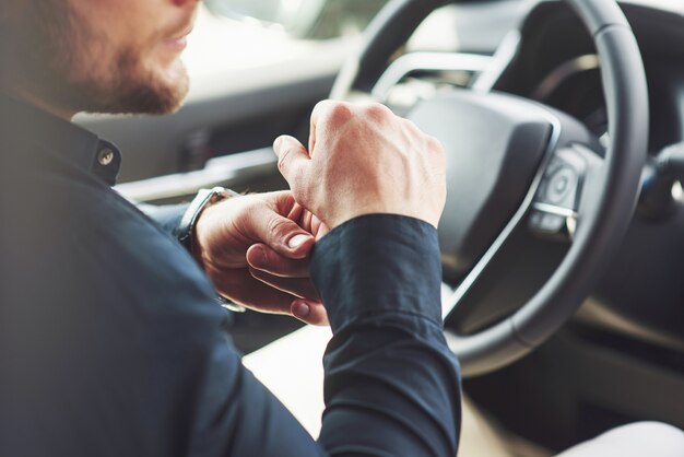 Un empresario monta su coche, se mueve sobre el volante. Mano con reloj.