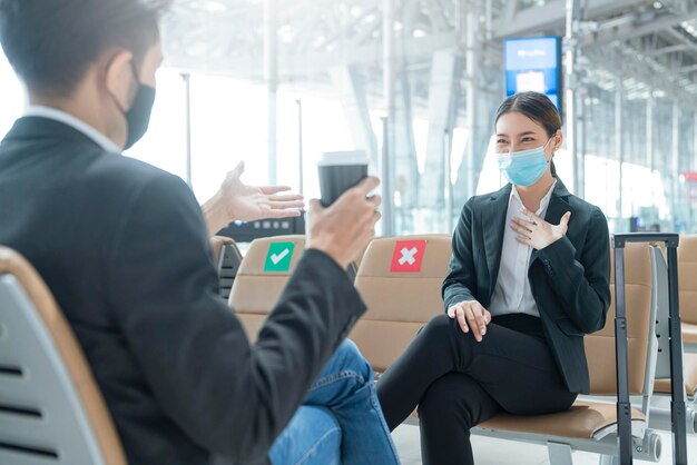 Empresario y mujer con protección de mascarilla facial reunión informal con asiento de distanciamiento social en la terminal del aeropuerto nuevo concepto de negocio de estilo de vida