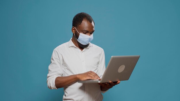 Empresario navegando por el sitio web de Internet en una computadora portátil, trabajando en una aplicación de redes sociales durante la pandemia del coronavirus. Adulto joven que sostiene un dispositivo inalámbrico moderno para buscar datos en línea.