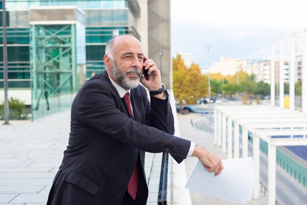 Empresario de pelo gris pensativo positivo hablando por teléfono celular