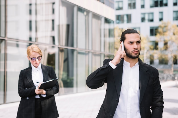 Empresario de pie frente a la empresaria ocupada hablando por teléfono celular