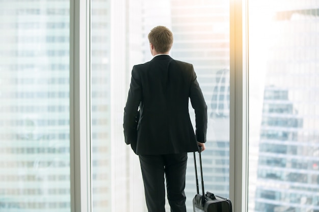 Empresario de pie con la maleta cerca de la ventana