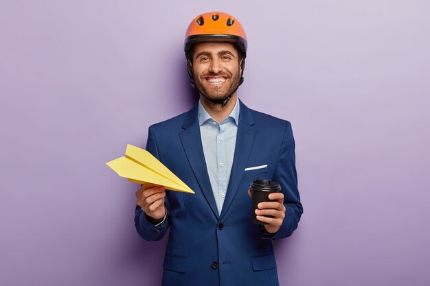 Empresario positivo posando en elegante traje y casco rojo en la oficina