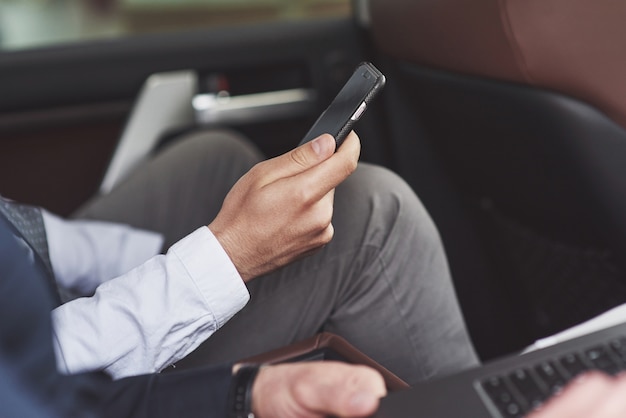 Un empresario que envía un mensaje a un teléfono inteligente y se dirige al asiento trasero del automóvil.