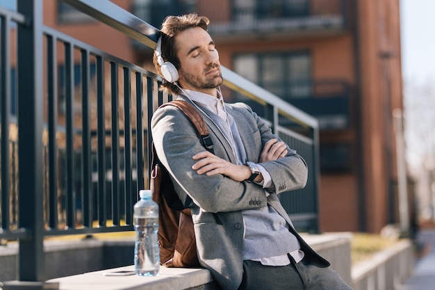 Empresario relajado con los ojos cerrados escuchando música con auriculares en la calle