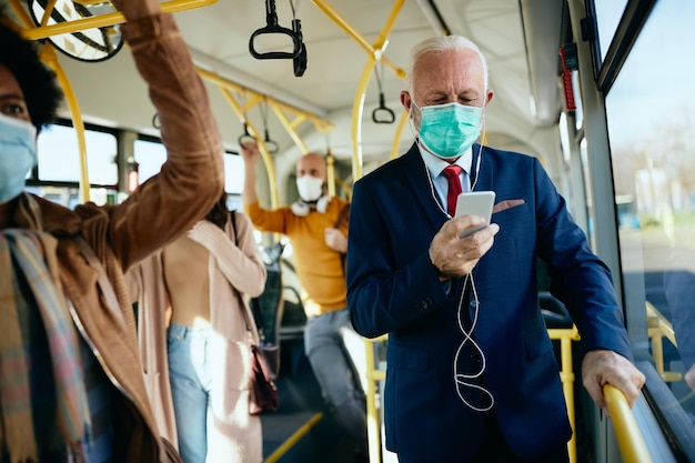 Empresario senior con mascarilla usando un teléfono inteligente en un transporte público