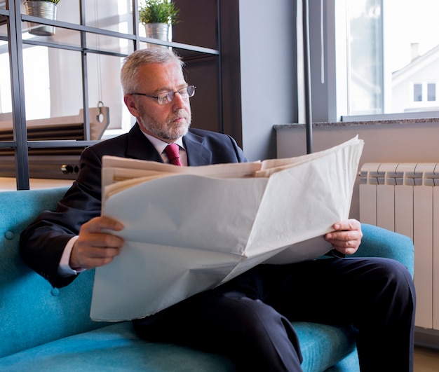 Foto gratuita empresario senior sentado en el sofá leyendo el periódico en la oficina