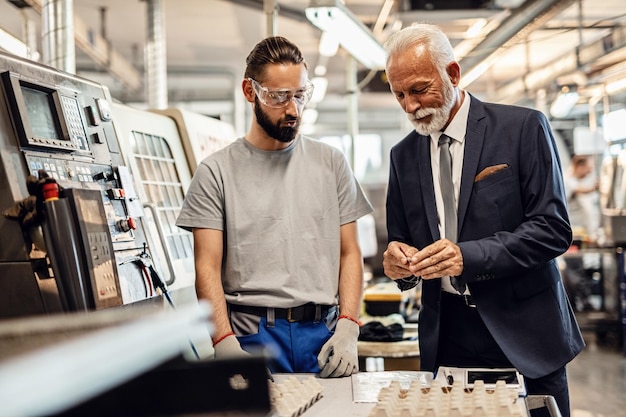 Empresario senior visitando la planta de la fábrica y examinando los productos fabricados con el trabajador de la instalación