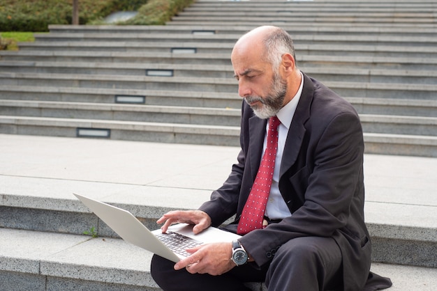 Empresario serio con computadora portátil en la calle