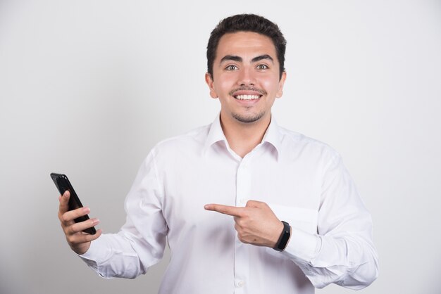 Empresario sonriente apuntando al teléfono sobre fondo blanco.