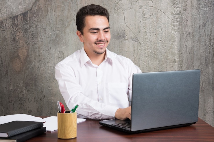 Foto gratuito empresario sonriente mirando a la computadora portátil y sentado en el escritorio. foto de alta calidad