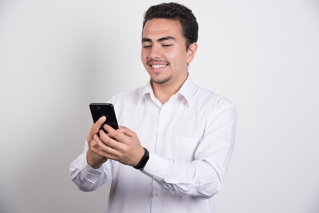 Empresario sonriente mirando teléfono sobre fondo blanco.