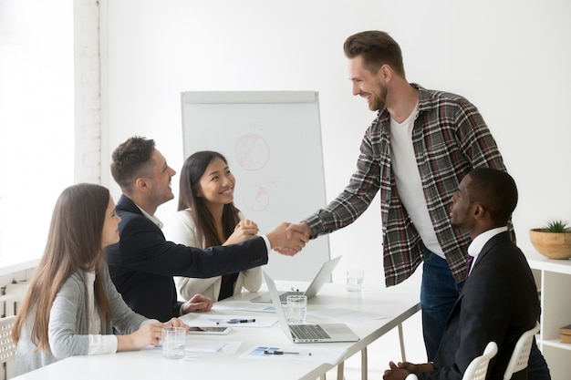 Empresario sonriente que da la bienvenida a un nuevo socio en una reunión de grupo con un apretón de manos