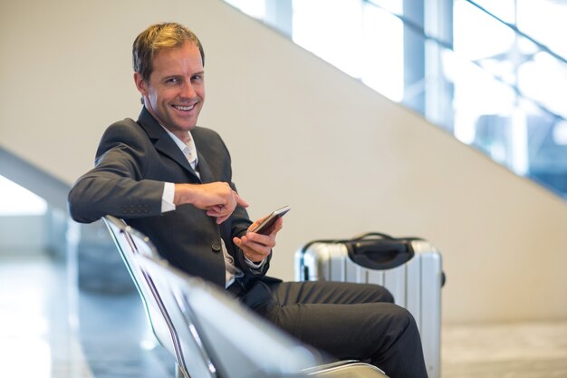 Empresario sonriente sentado con teléfono móvil en la sala de espera