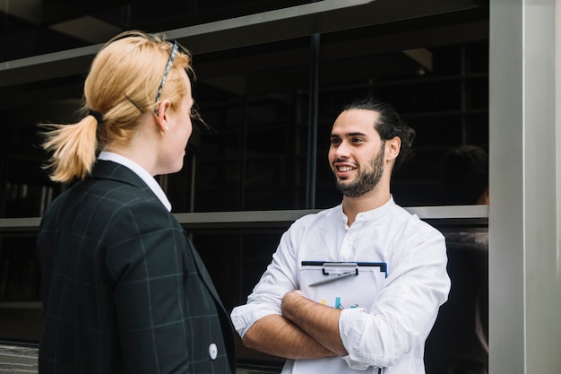 Foto gratuita empresario sonriente sosteniendo portapapeles hablando con empresaria