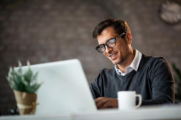 Empresario sonriente trabajando en una laptop mientras está sentado en el escritorio de la oficina