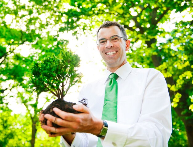 Empresario sosteniendo un árbol para plantar en un bosque.