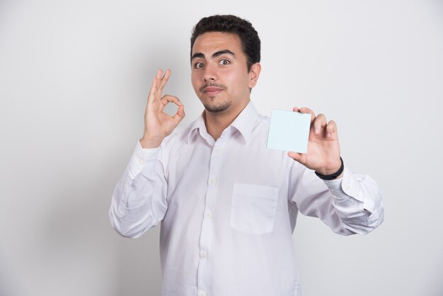 Empresario sosteniendo blocs de notas y mostrando signo ok sobre fondo blanco.