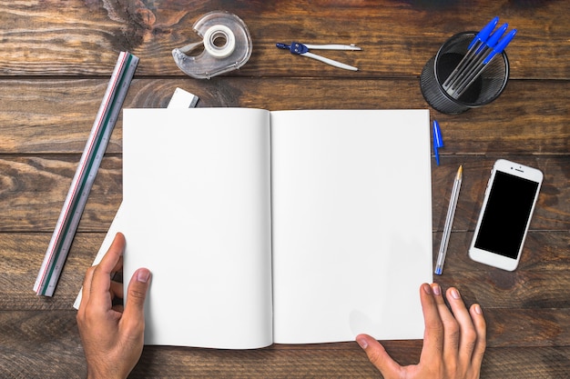 Foto gratuita empresario sosteniendo el libro blanco rodeado de artículos de papelería y teléfono móvil