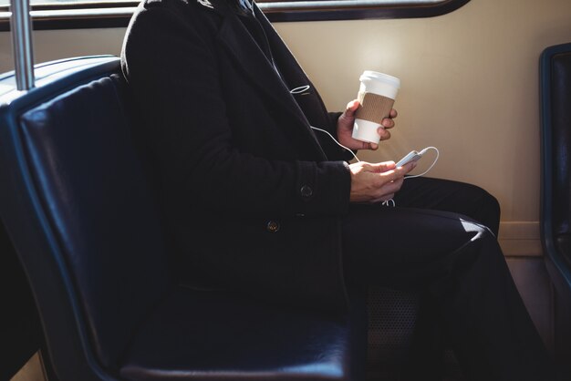 Empresario sosteniendo una taza de café desechable y utilizando el teléfono móvil